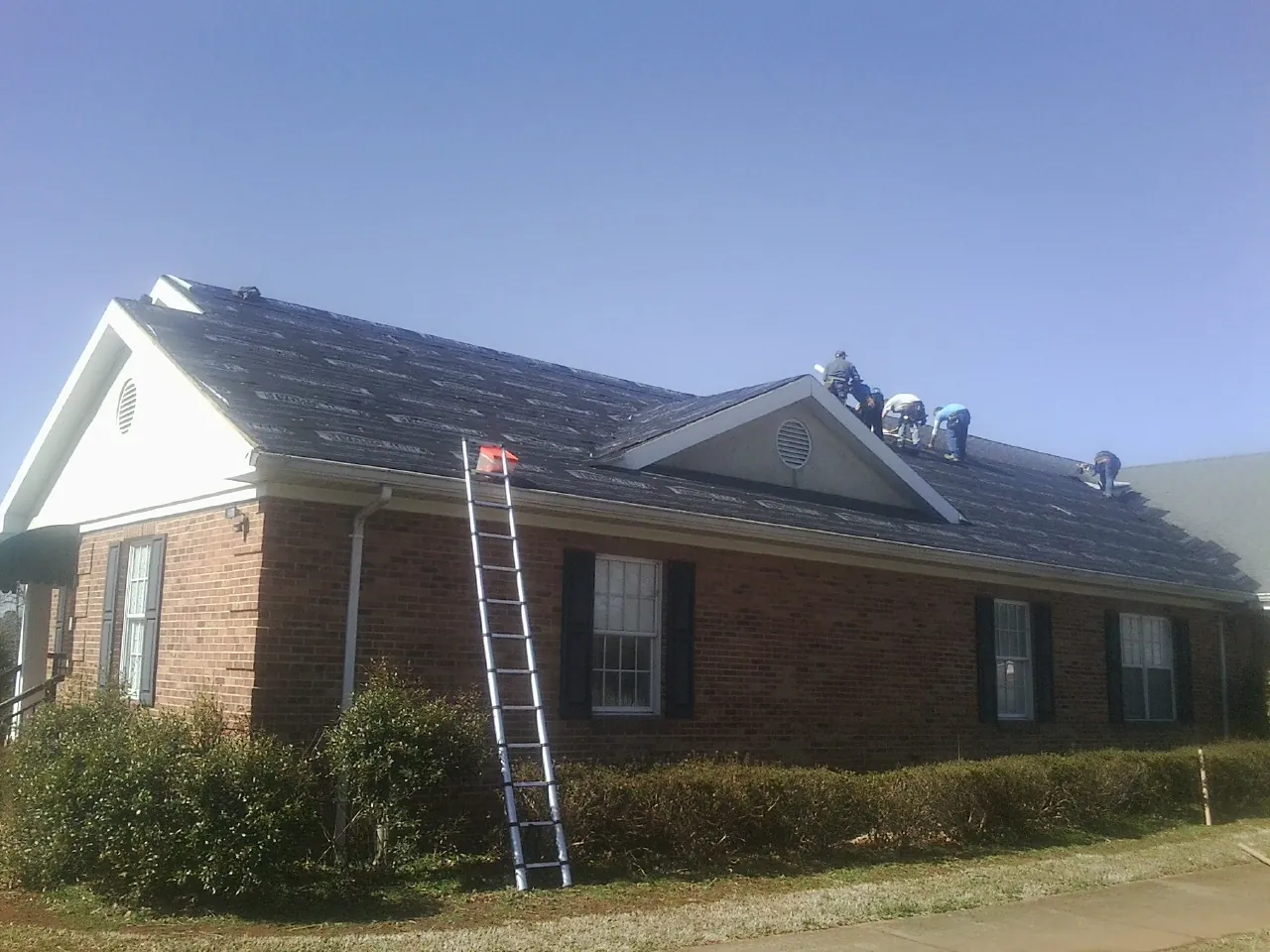 Crew tearing shingles off a brick ranch roof with a ladder set — Emergency Roof Repair work by our crew in Brainerd
