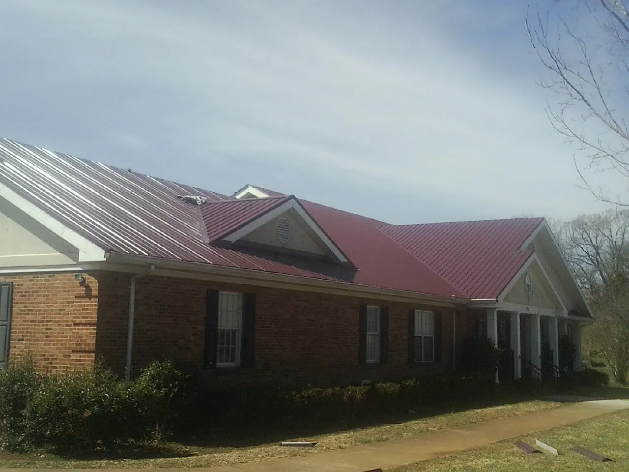 Red metal roof with gabled entries on a long brick building, from a Hail Damage Roof Repair job in Brainerd