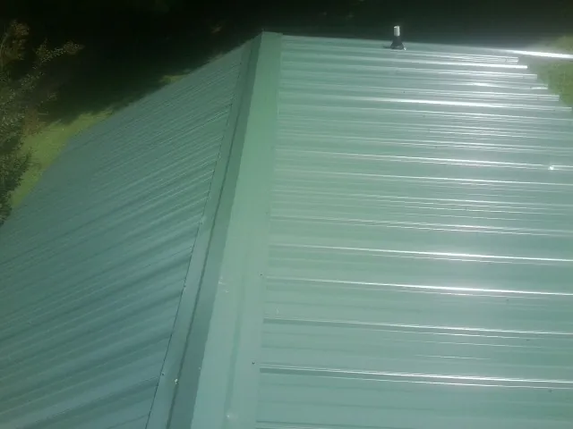 New green metal panels meeting at the ridge of a roof — Flat Roof Repair work by our crew in Brainerd