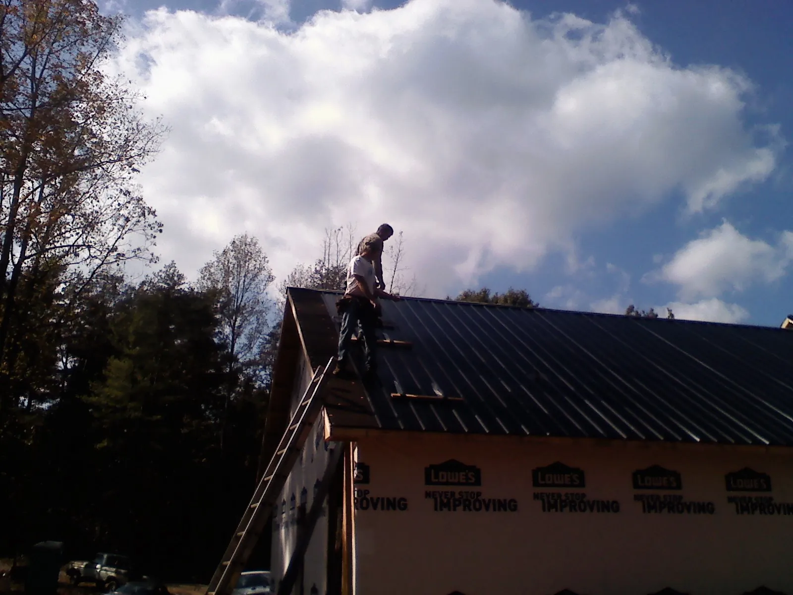 Roofer fastening dark metal panels high against a cloudy sky, from a Roof Inspection job in Brainerd