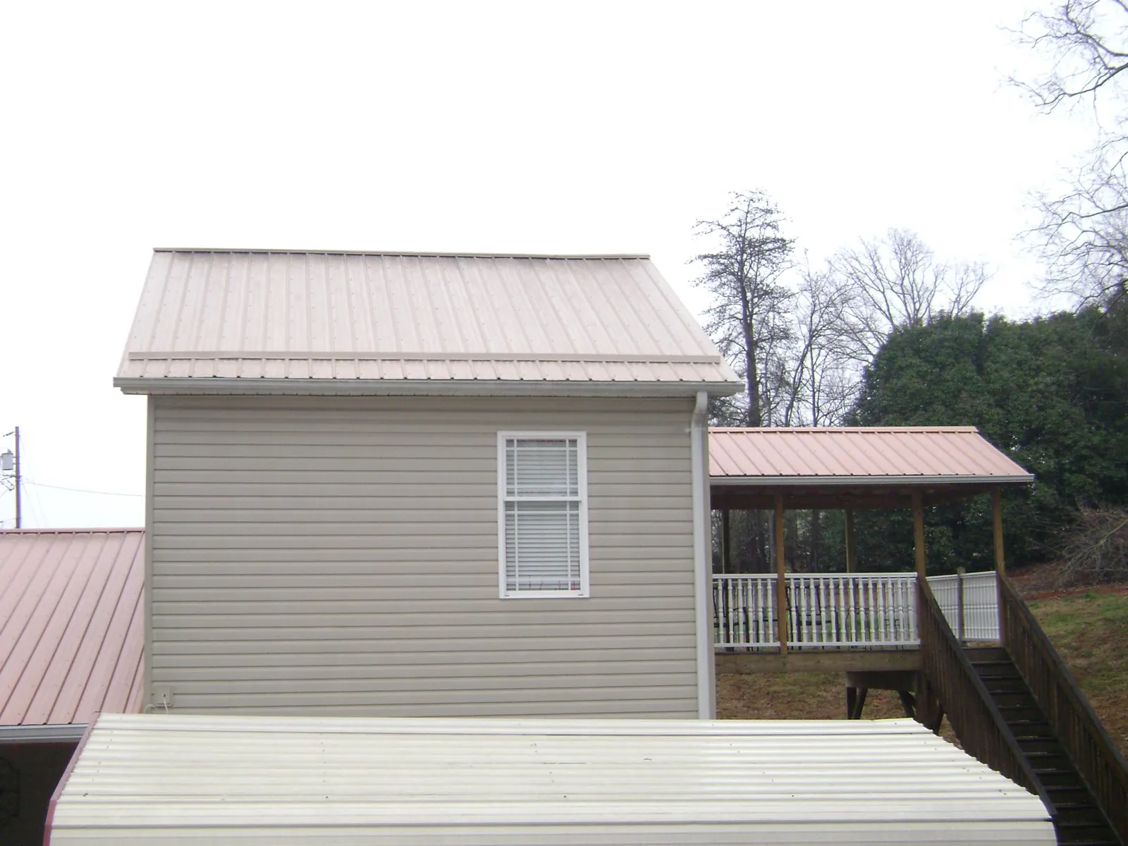 Tan metal roofs on a two story addition and attached porch, from a Roof Replacement job in Brainerd